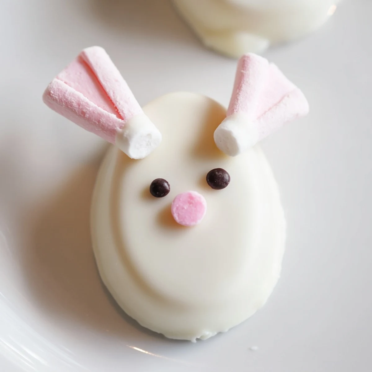 White chocolate-dipped bunny Oreo balls with pink marshmallow ears and tails arranged on a festive Easter dessert platter