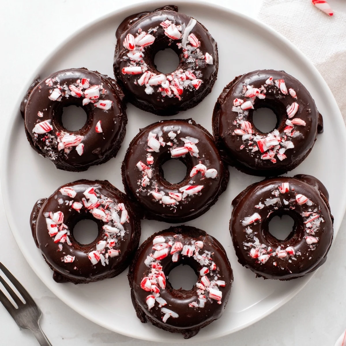 Chewy gluten-free chocolate donuts with peppermint flavor drizzled with chocolate glaze and festive peppermint sprinkles