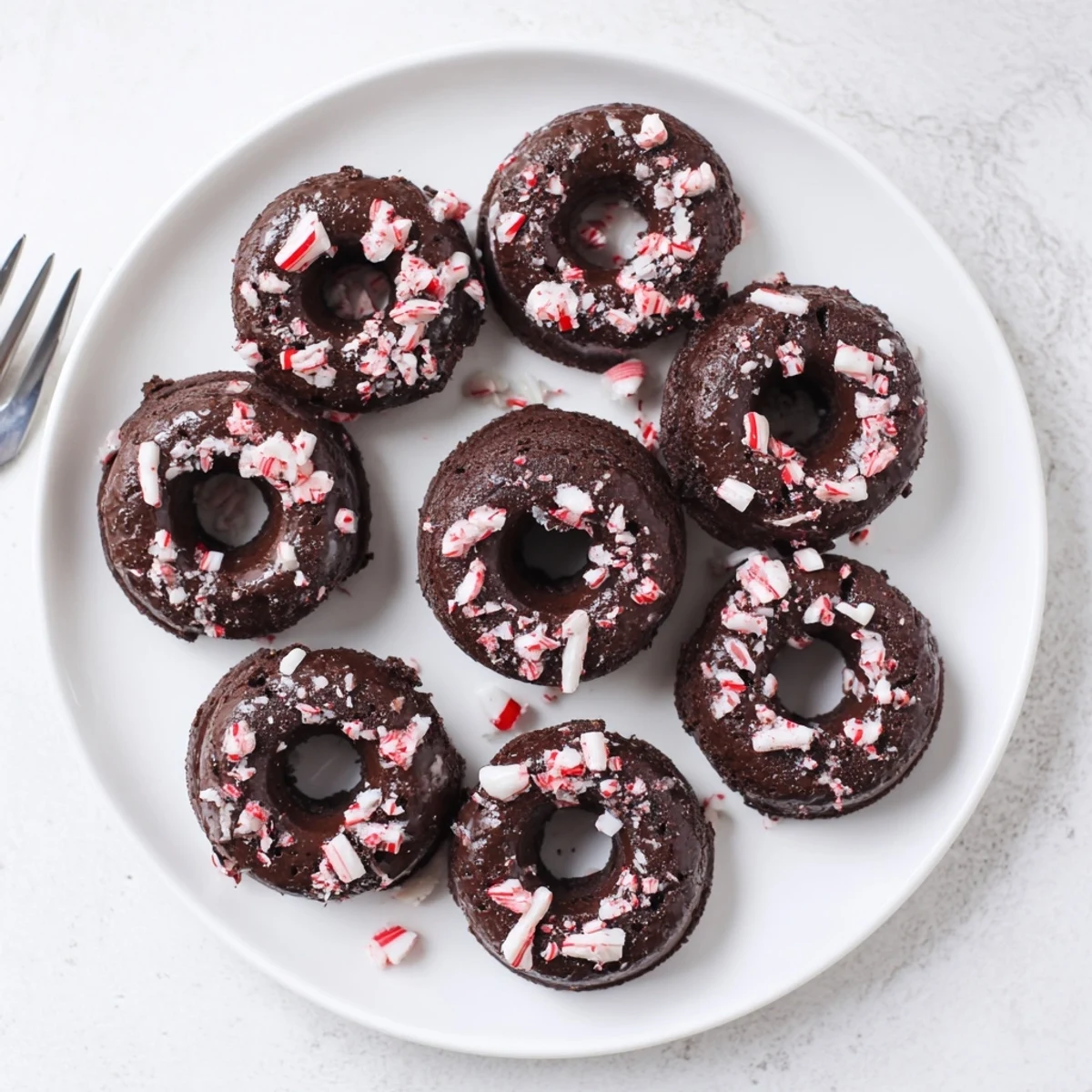 Homemade chocolate peppermint mochi donuts arranged on a wire rack with glossy glaze and candy cane topping