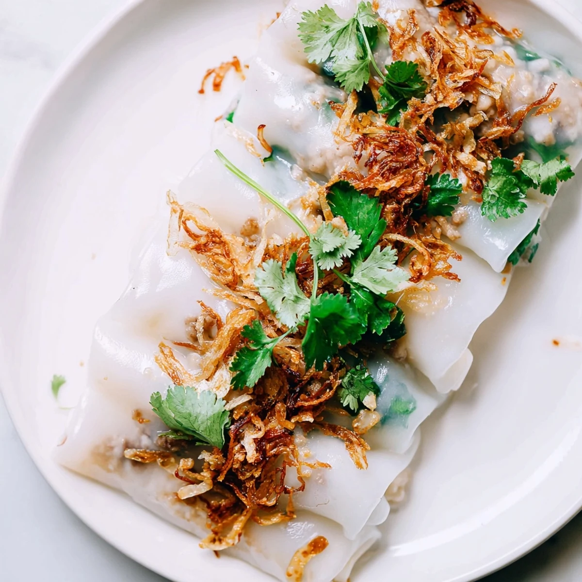 Steamed Vietnamese Banh Cuon featuring silky rice wrappers topped with fried shallots and fresh herbs