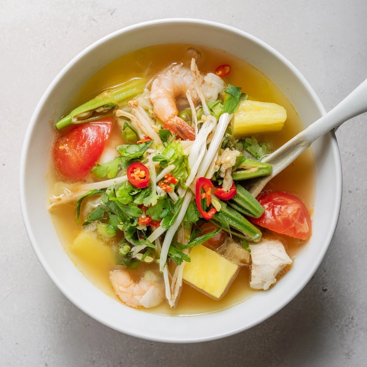 Golden bowl of Vietnamese Canh Chua soup with tender fish chunks, pineapple, and fresh green herbs garnish