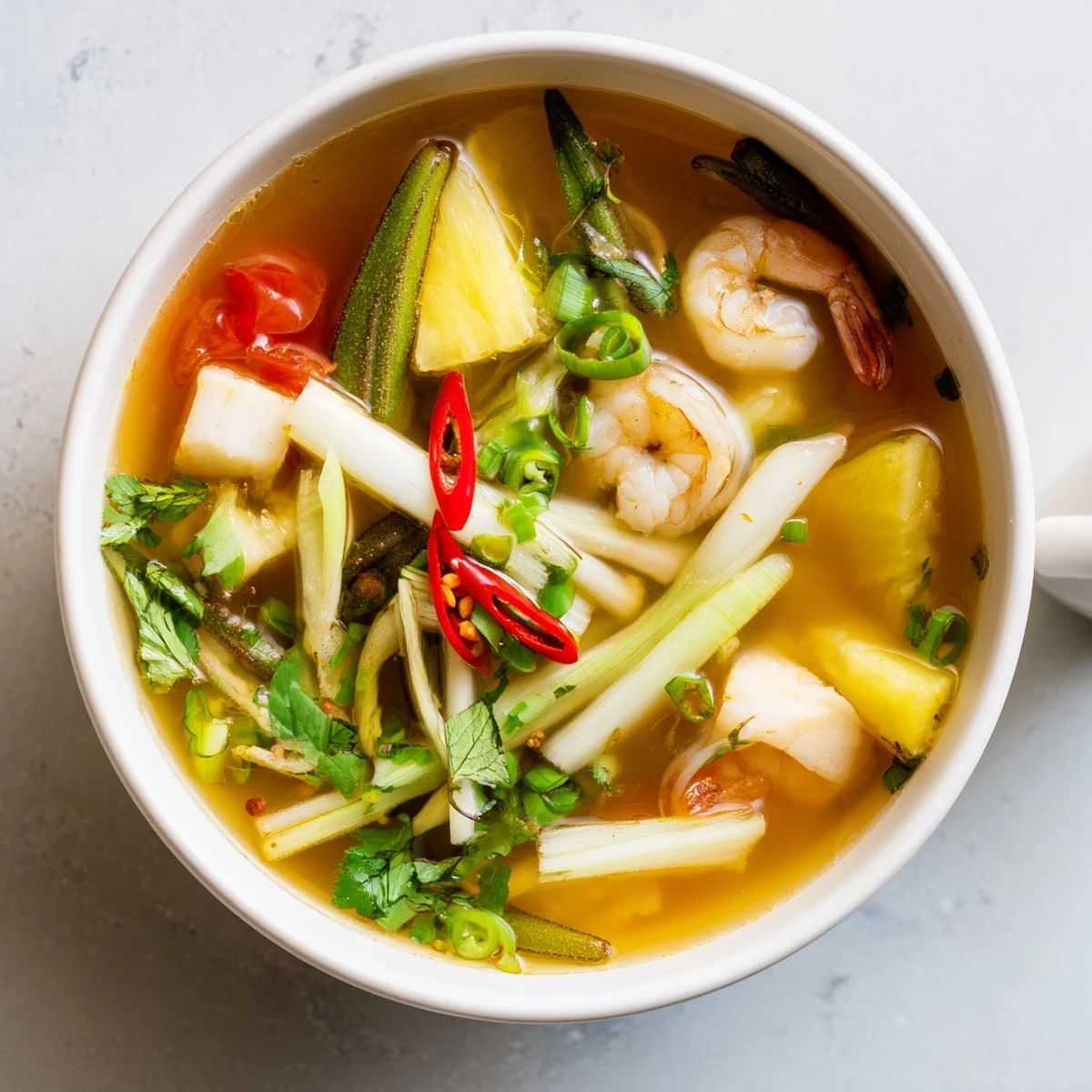 Steaming Canh Chua sweet and sour soup featuring catfish, pineapple wedges, and vibrant cilantro in a ceramic bowl