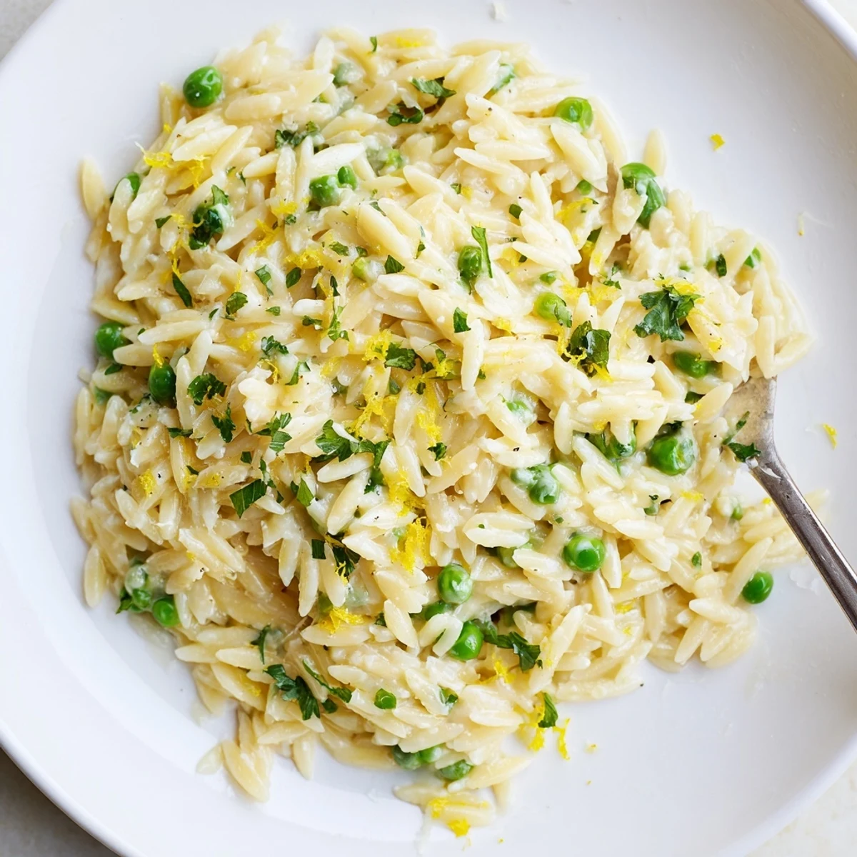 Creamy lemon orzo plated with vibrant green herbs and lemon zest garnish on rustic surface