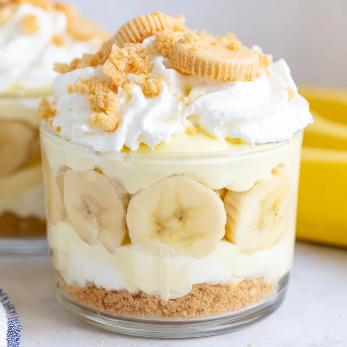 Individual no bake banana pudding cheesecake cups topped with golden wafer crumbs and sliced bananas
