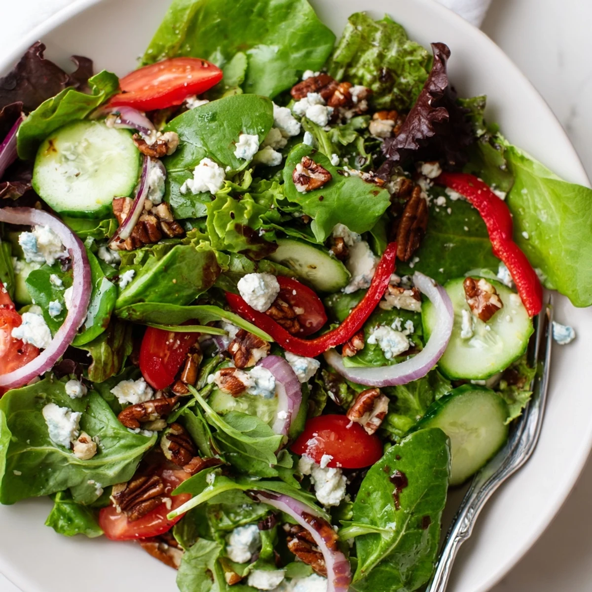 Crisp spring mix salad featuring baby greens, sliced cucumbers, tomatoes, and crumbled feta cheese