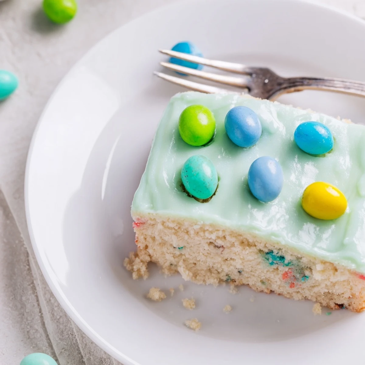 Slices of moist Robin Egg Snack Cake garnished with speckled malted candies on pastel icing