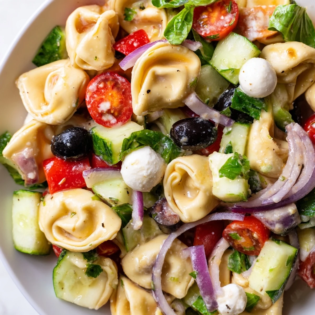 Creamy cheese tortellini salad loaded with crisp vegetables and olives in a vibrant serving bowl