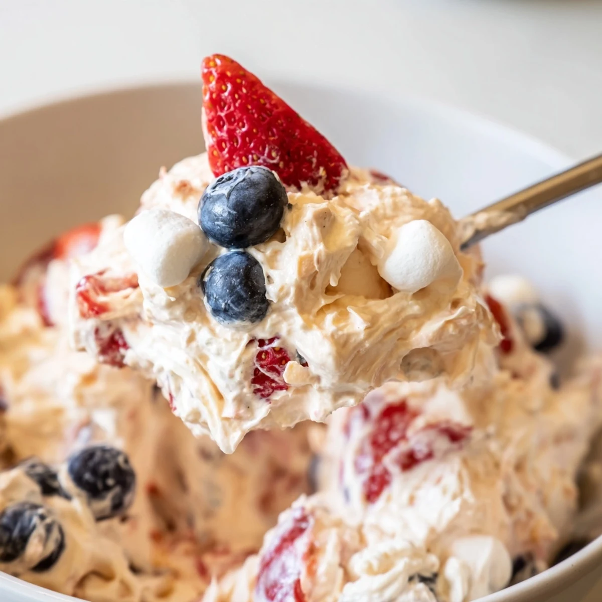 Creamy red white blue cheesecake salad loaded with fresh berries and marshmallows in a glass bowl