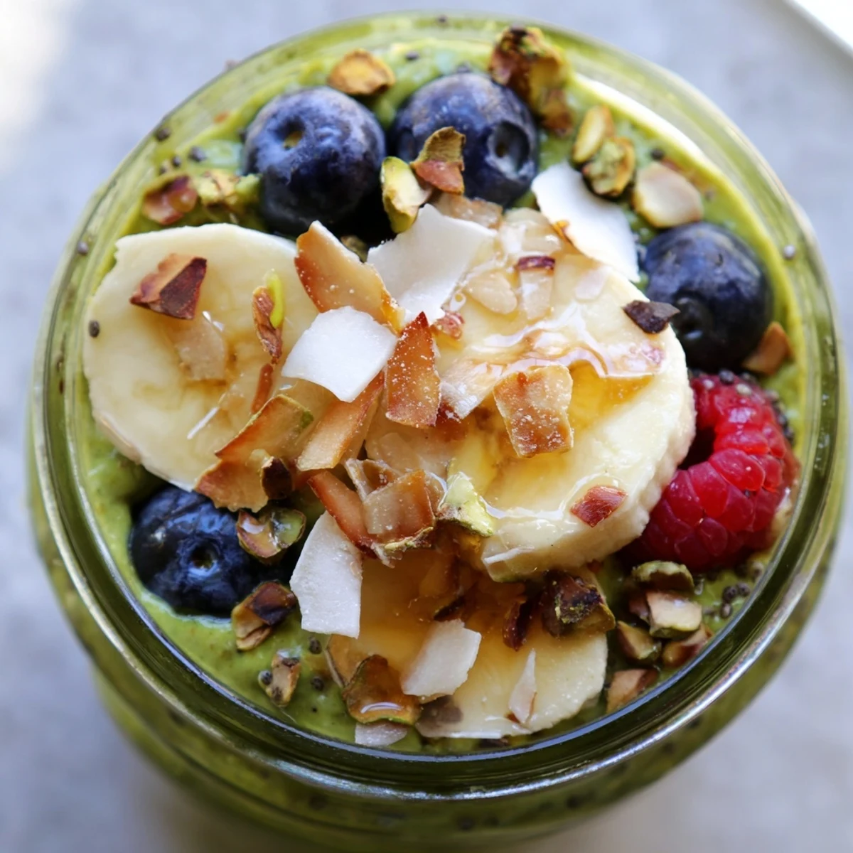 Thick matcha overnight oats served in a glass jar layered with sliced banana and pistachios