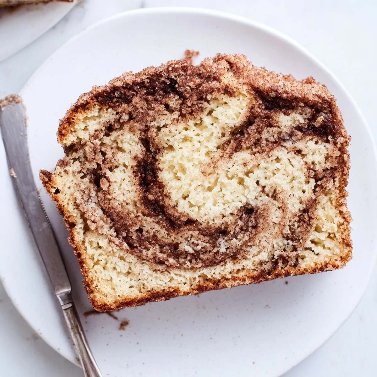 Golden snickerdoodle banana bread loaf sliced on a rustic cutting board with a cinnamon-sugar swirl visible inside