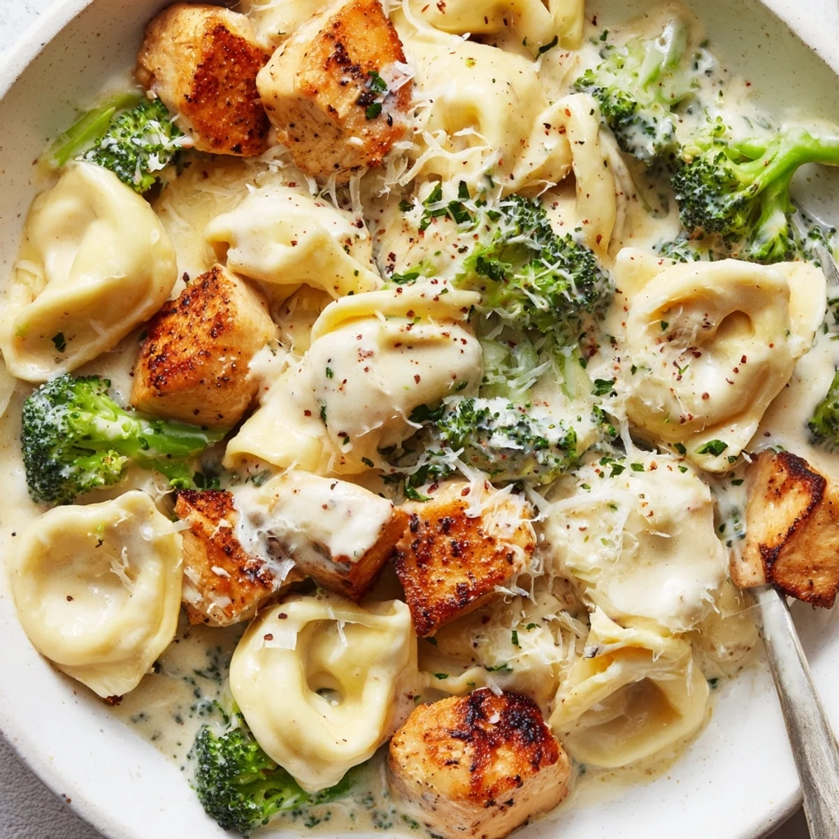 Skillet full of steaming Creamy Garlic Parmesan Tortellini Chicken Broccoli Recipe, fragrant and rich.