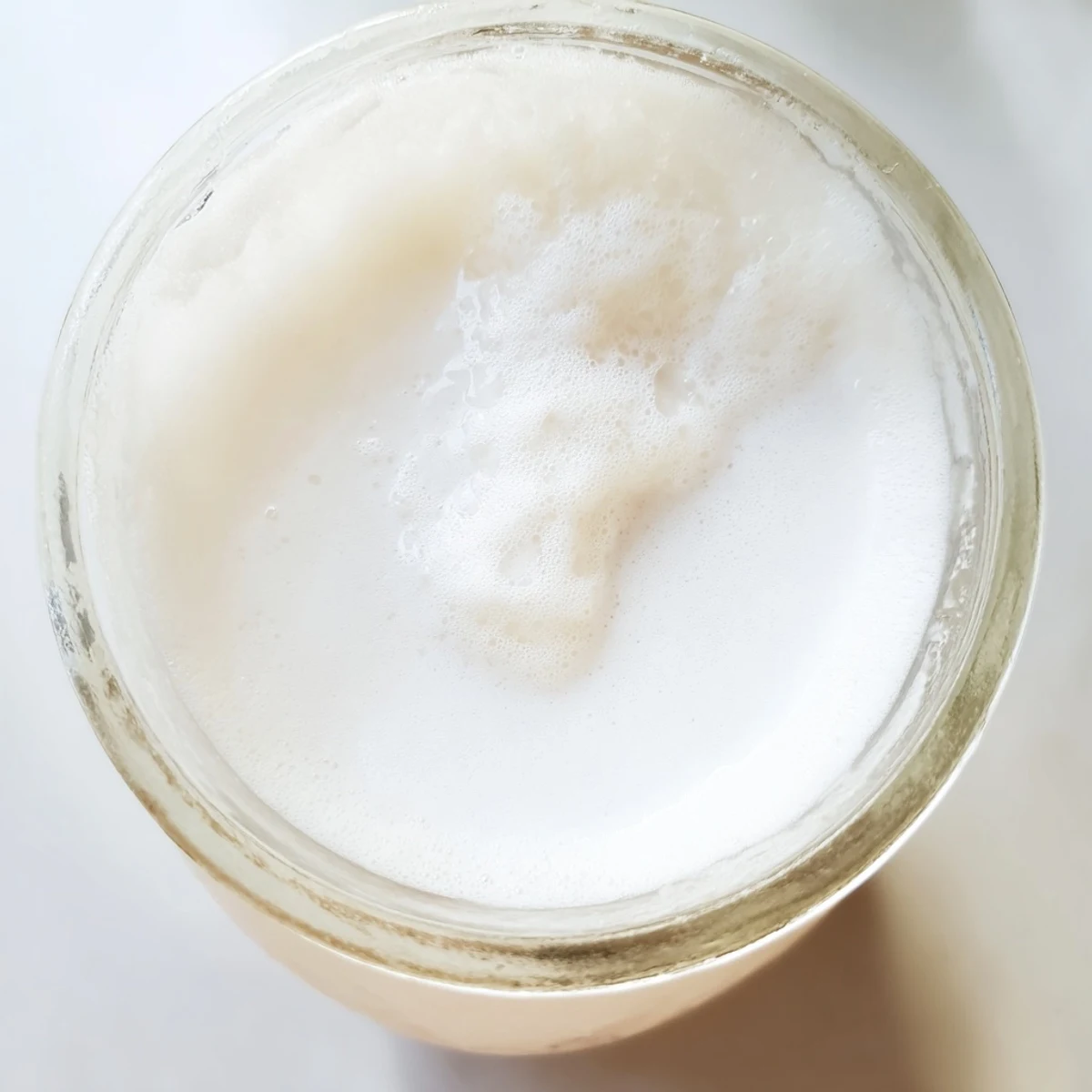 Glass bottle of DIY coconut milk poured into a bowl with nut milk bag straining setup