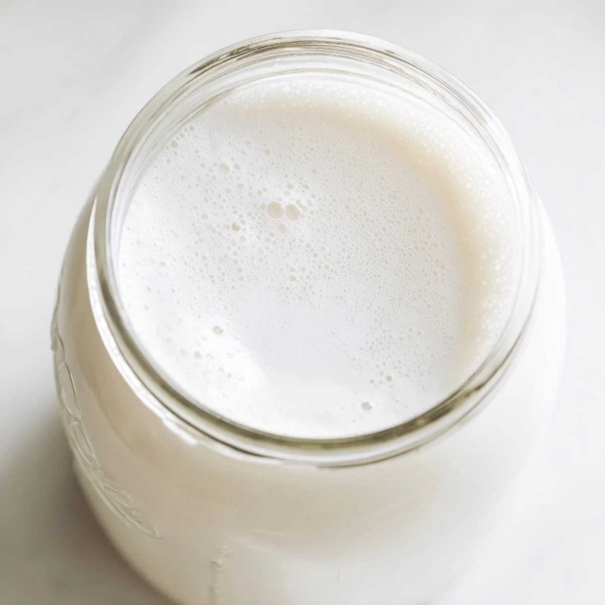 Fresh homemade coconut milk in a glass jar with creamy white texture and visible coconut flakes