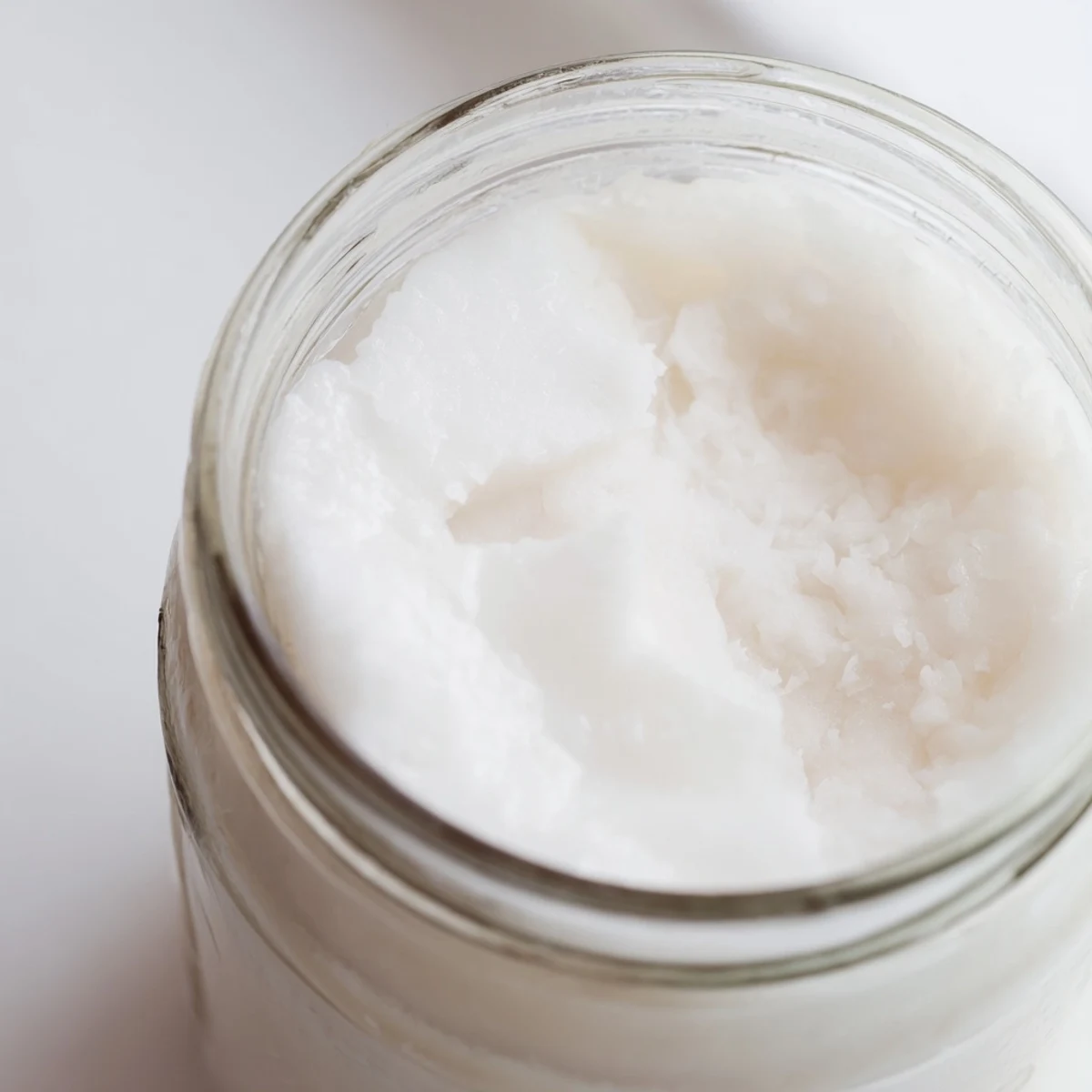 Rich coconut milk in mason jar surrounded by dried coconut on wooden kitchen counter