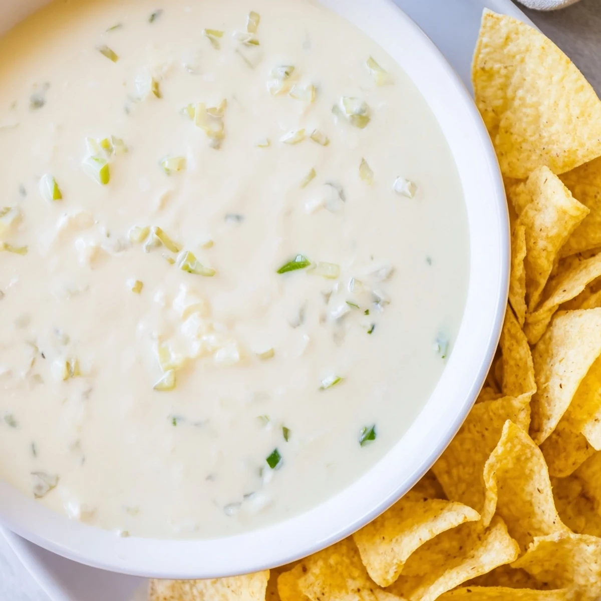 Warm white queso dip poured generously over tortilla chips, perfect for party appetizer spreading