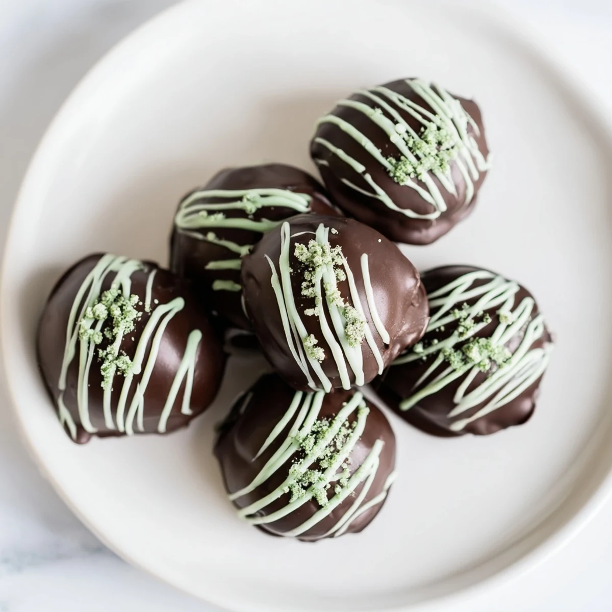 Rich homemade mint Oreo truffles displayed on a white plate with chocolate drizzle
