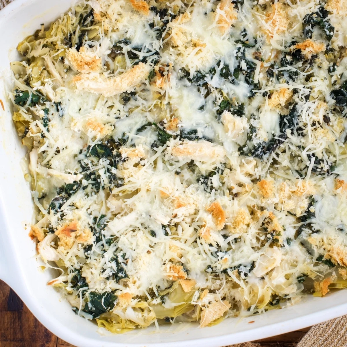 Hearty high protein spinach and artichoke chicken casserole served in a white baking dish
