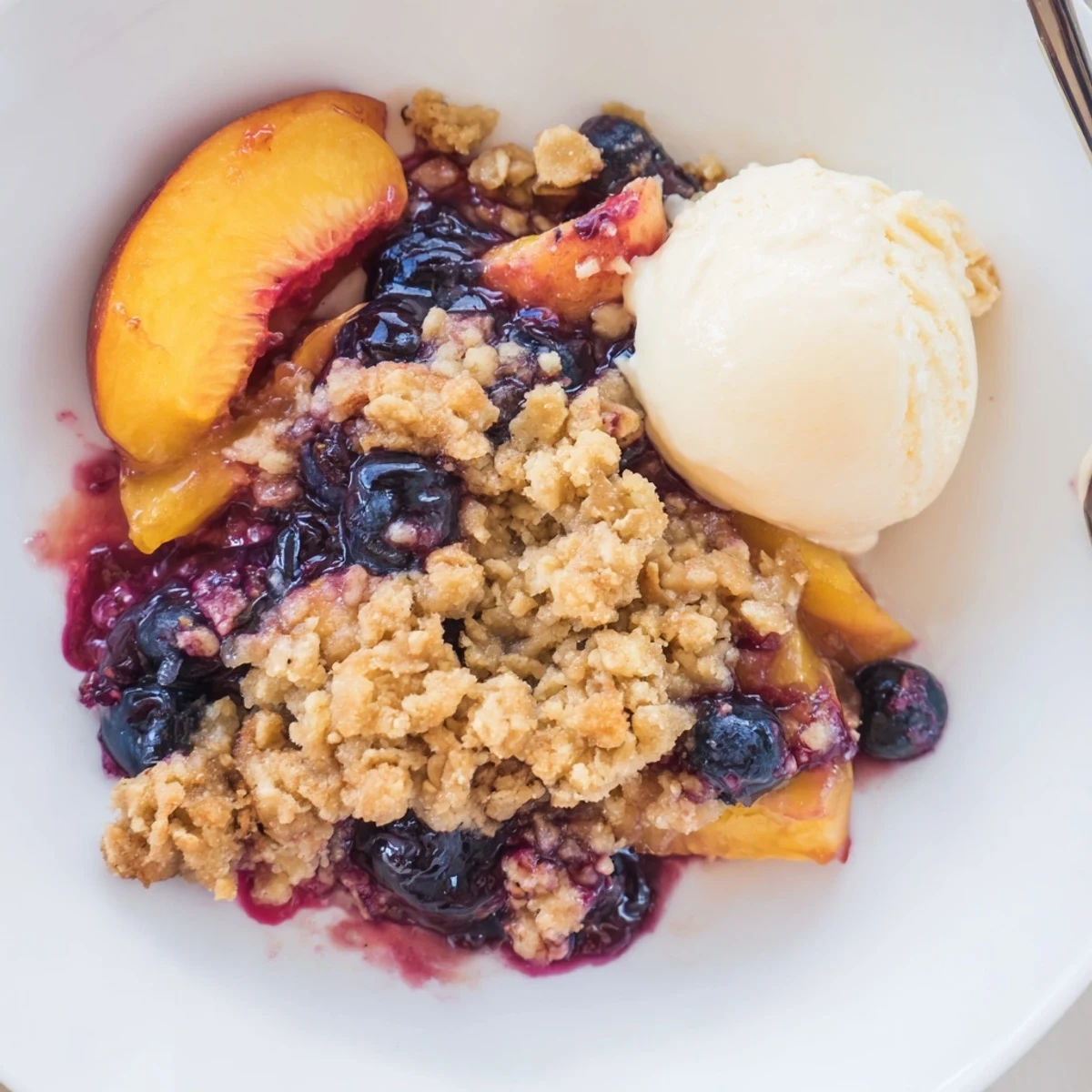 Blueberry Peach Crumble bubbling golden, warm from oven with melting vanilla ice cream