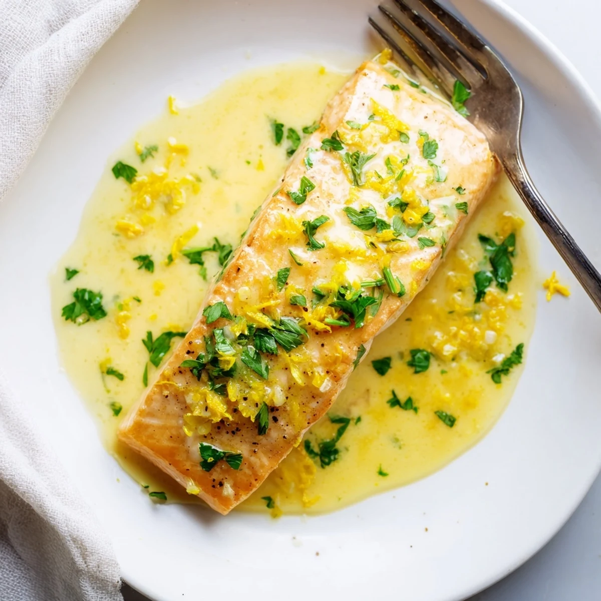 Perfectly cooked salmon fillet topped with tangy lemon cream sauce garnished with lemon zest and parsley