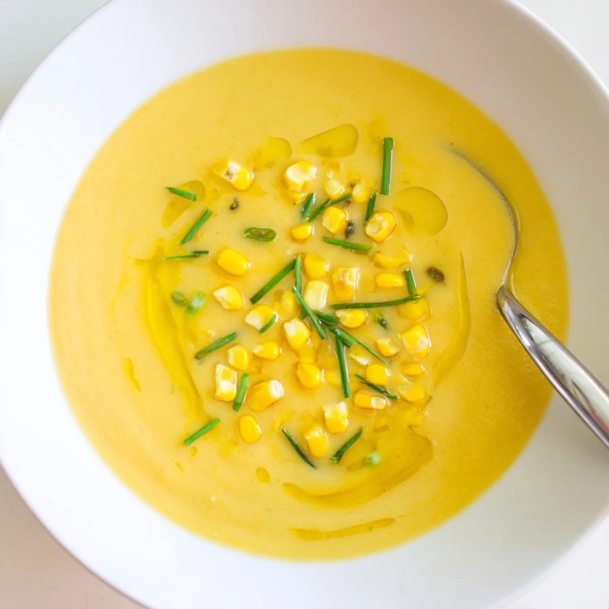 Vibrant summer sweet corn gazpacho poured into shallow bowls alongside crusty bread for dipping